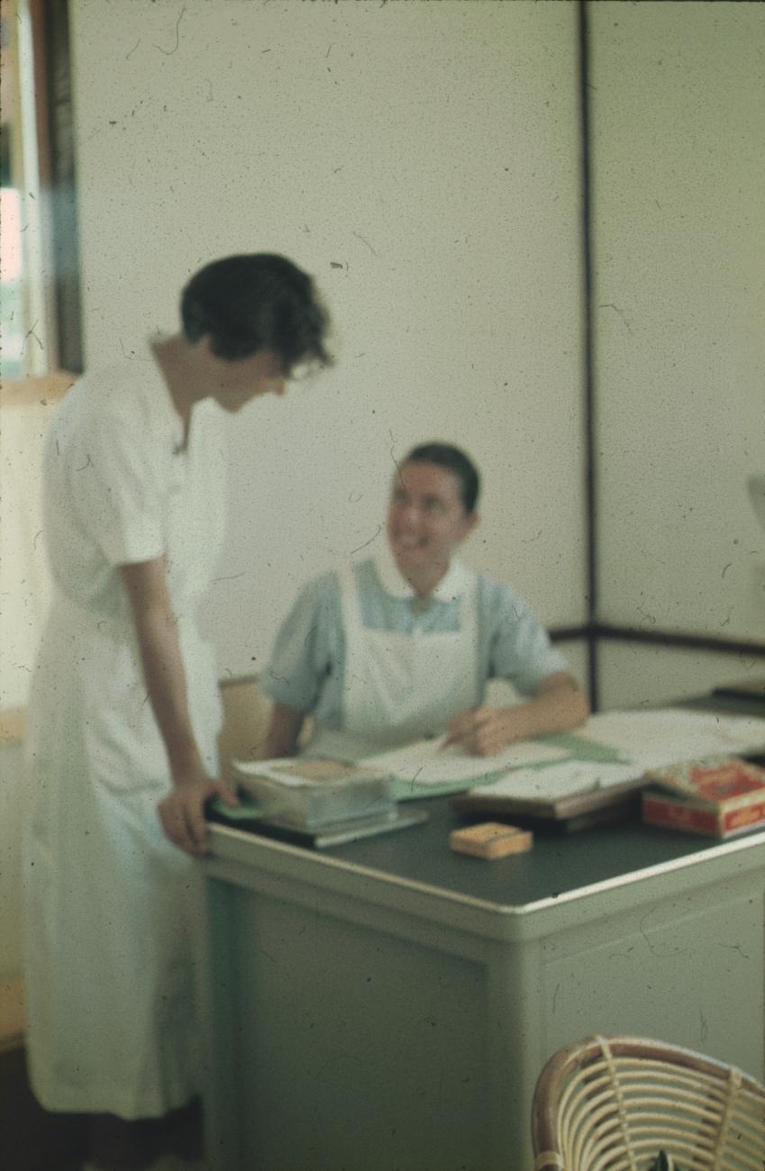 BD/171/597 - 
Twee verpleegsters bij een bureau.
