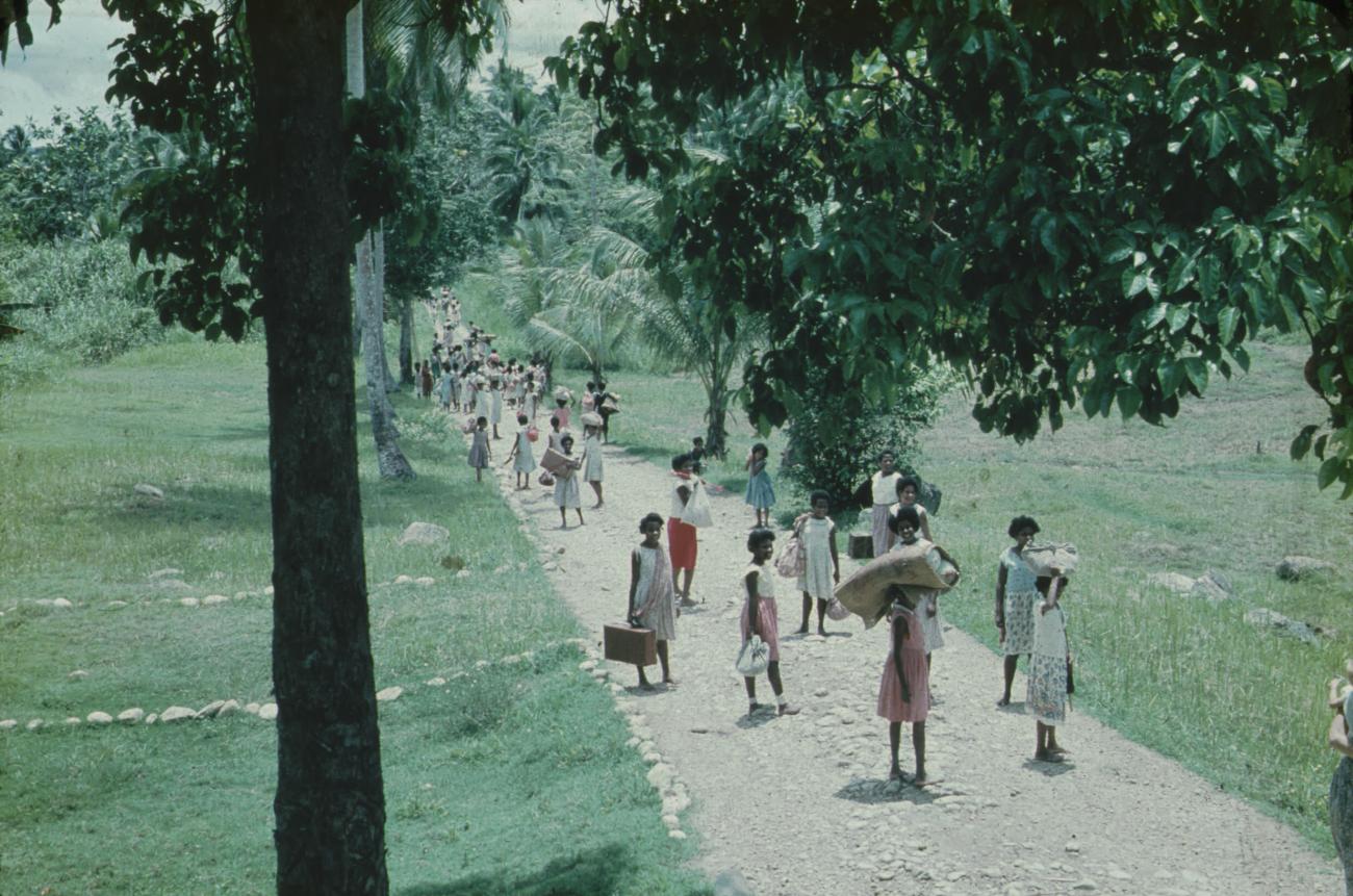 BD/171/1356 - 
Vrouwelijke leerlingen met bagage lopend over weg.
