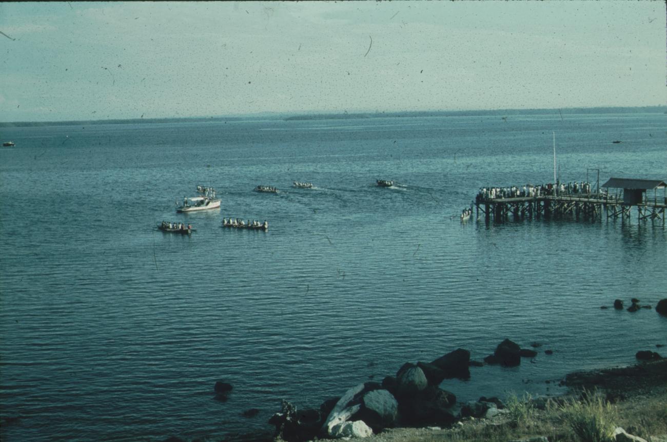 BD/171/649 - 
Aanlegsteiger met mensen, prauwen en schip in baai.
