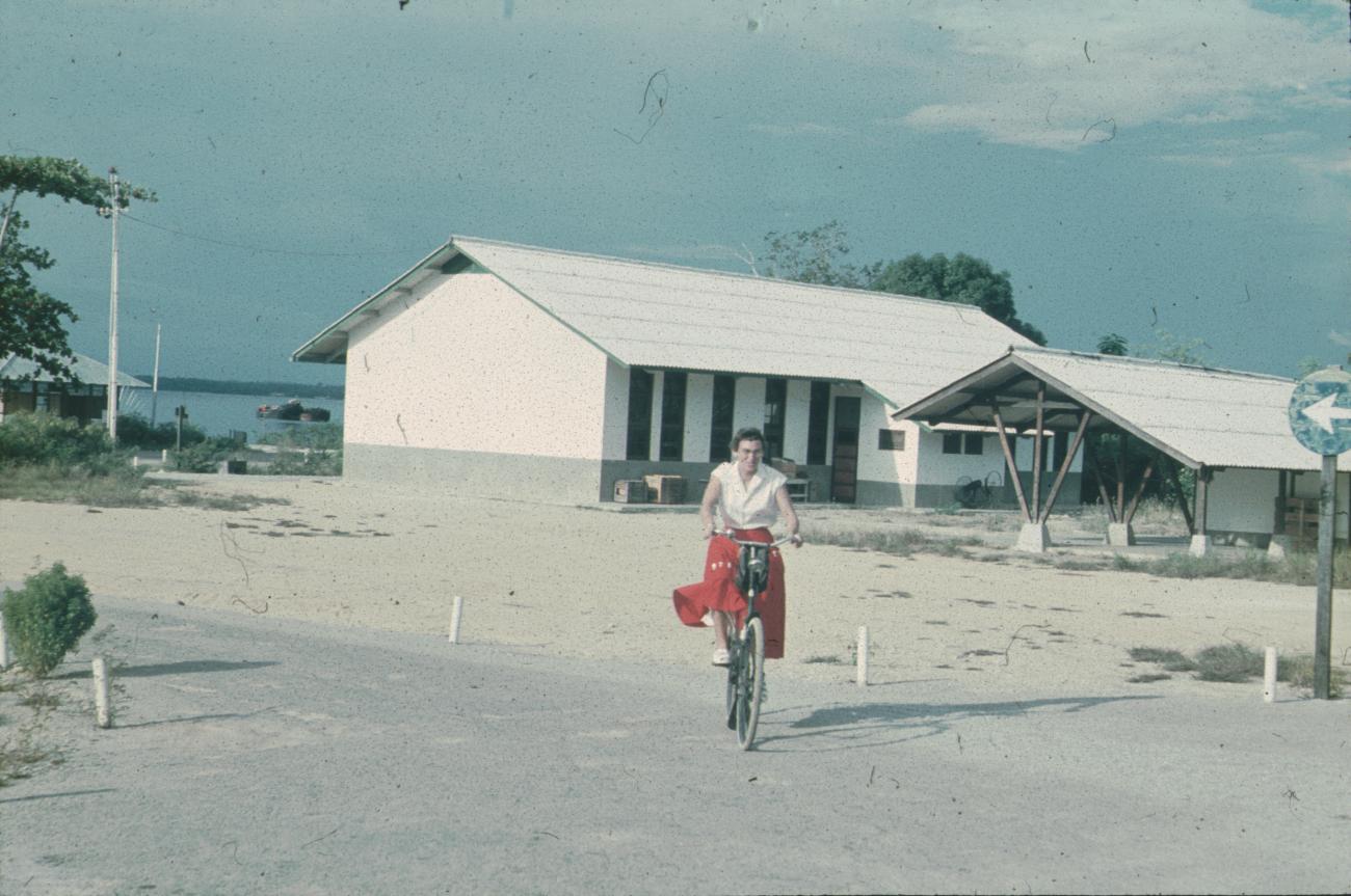 BD/171/667 - 
Westerse vrouw op fiets, gebouwen op achtergrond.
