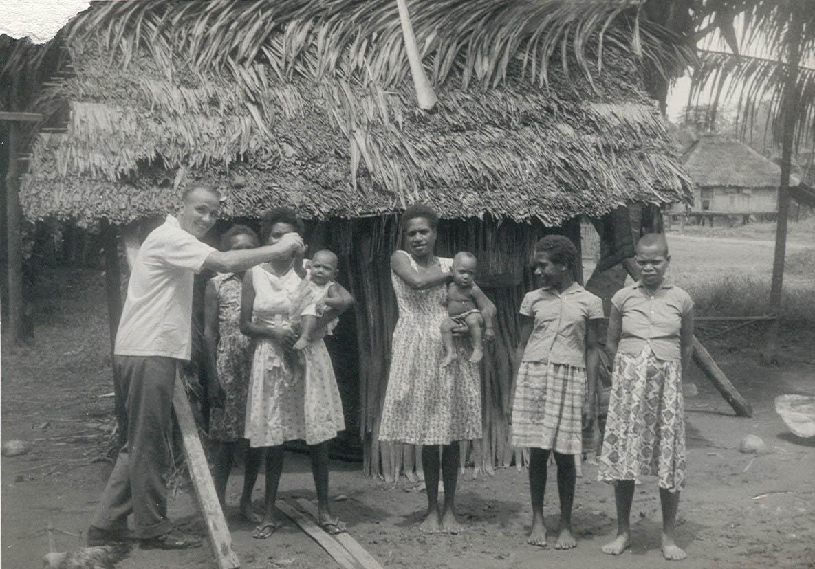 BD/269/1152 - 
Franciscaans broeder Henk Blom met Papoea-vrouwen en meisjes poserend voor hun woning
