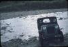 BD/171/274 Een jeep rijdt door stromende rivier bezaaid met kiezelstenen en keien