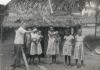 BD/269/1152 Franciscaans broeder Henk Blom met Papoea-vrouwen en meisjes poserend voor hun woning